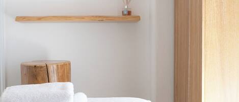 A neatly arranged bedroom with a bed, two wall mirrors, a wooden shelf with a small decorative item, and a wooden stool.