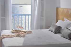 Habitación de hotel con cama, una bandeja con vasos y una botella, y vista al mar.