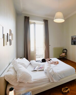 Un lit bien fait, avec du linge de lit blanc, un luminaire suspendu, un radiateur et un tableau encadré au mur.