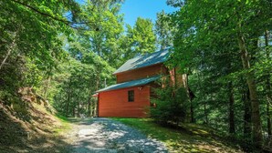 Un chalet rustique, accessible par un chemin de gravier, entouré d’une forêt dense.