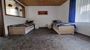 A bedroom with two wooden beds, a tiled floor, a painting on the wall, and a window with blue curtains. - W.I.L.A. 3 (Helmbrechts)