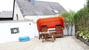 An outdoor seating area with a table and chairs, a blue trash bin, and a white wall. - W.I.L.A. 3 (Helmbrechts)