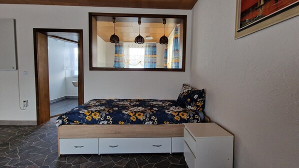A bedroom with a bed, a bedside table, a wardrobe, a mirror, and a window with curtains.