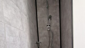 A narrow shower stall with grey tiles and a black floor, equipped with a handheld showerhead and a wall-mounted faucet. - W.I.L.A. 3 (Helmbrechts)