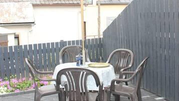 Un patio al aire libre con una mesa redonda y cuatro sillas, rodeado de un piso de ladrillo y una valla de madera.