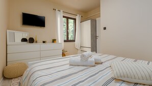Une chambre à coucher avec un lit, un téléviseur fixé au mur, une fenêtre avec des rideaux, une table de chevet avec une lampe et une porte donnant sur une autre pièce.