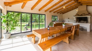Un vaste espace dédié à la salle à manger, avec une grande table et des bancs en bois, une cheminée et de grandes fenêtres offrant une vue sur l’extérieur.