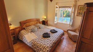 Une chambre avec un grand lit, une table de chevet, une lampe, une fenêtre donnant sur un paysage verdoyant et un fauteuil.