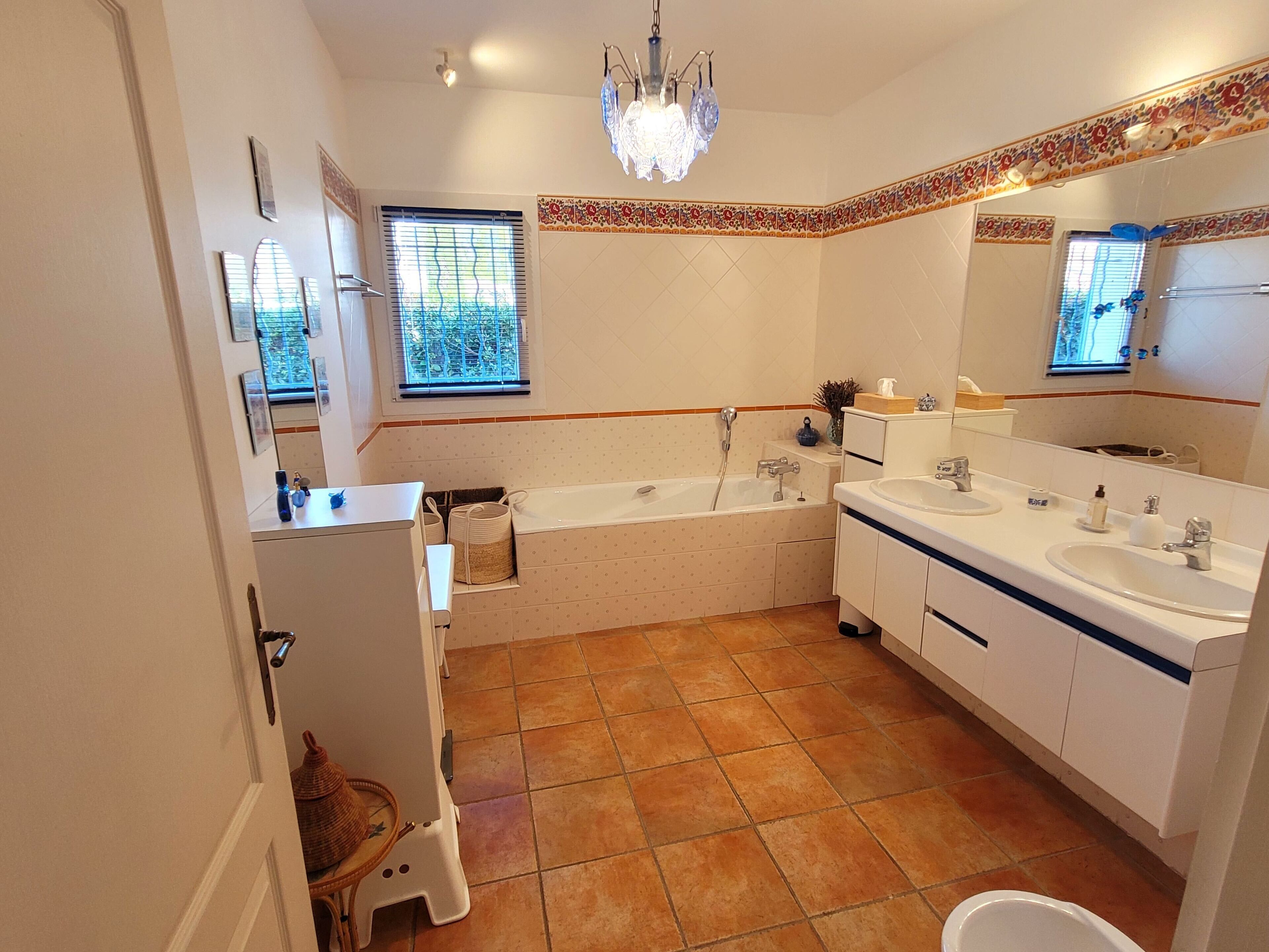 A modern bathroom with a large bathtub, two sinks, and a chandelier.