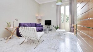 A modern living room with a purple sofa, a white chair, a TV, and a wooden cabinet. - SUPERIOR APARTMENT (Roma)