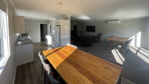 A spacious living area with a wooden dining table, a kitchen with a built-in washer and dryer, and a flat-screen TV mounted on the wall. - Lower Lodge (12 Bed) Pudding Hill (Methven)