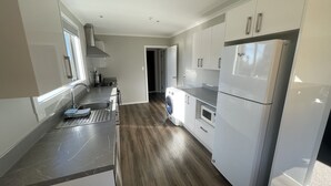 A modern kitchen with white cabinets, a stainless steel range hood, a built-in oven, and a refrigerator. - Lower Lodge (12 Bed) Pudding Hill (Methven)