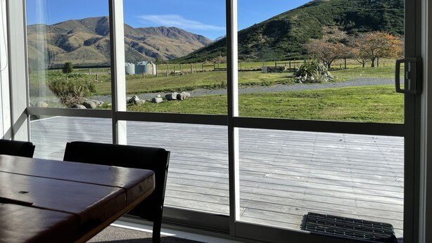 A room with a large window offering a view of a grassy landscape with hills and a fence. - Lower Lodge (12 Bed) Pudding Hill (Methven)