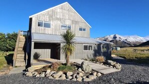A rustic wooden house with a garage, a wooden staircase, and a stone pathway leading to the entrance. - Lower Lodge (12 Bed) Pudding Hill (Methven)