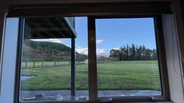 Una finestra con vista su un prato, alberi e una collina all'orizzonte.