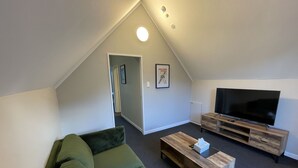 Un salon moderne avec un canapé vert, une table basse en bois et un téléviseur à écran plat posé sur un meuble en bois.