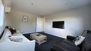 A modern living room with a white sofa, a black leather couch, a coffee table, and a flat-screen TV mounted on the wall. - Chalet 3 (5 Bed) Pudding Hill (Methven)