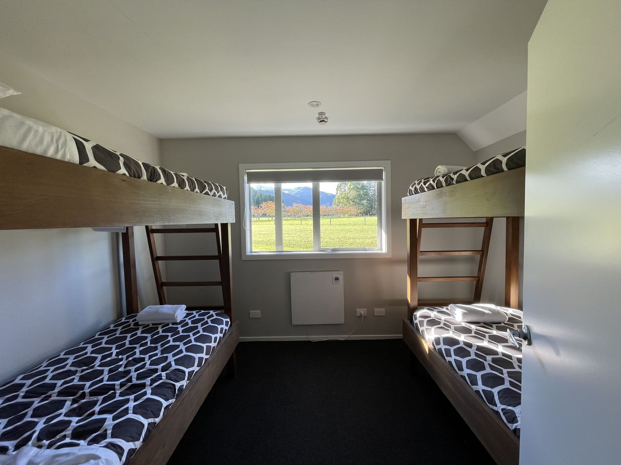 A room with two bunk beds, a window with a view of a grassy field and mountains, and a radiator on the wall.
