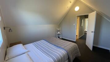 A bedroom with a bed, a nightstand, a ladder, and a door leading to another room.