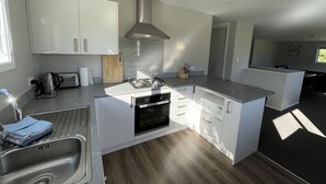 Een moderne keuken met witte kasten, een roestvrijstalen afzuigkap, een inbouwoven en een houten snijplank.