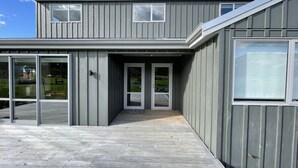 Een modern gebouw met twee verdiepingen, een overdekt houten terras en grote ramen.