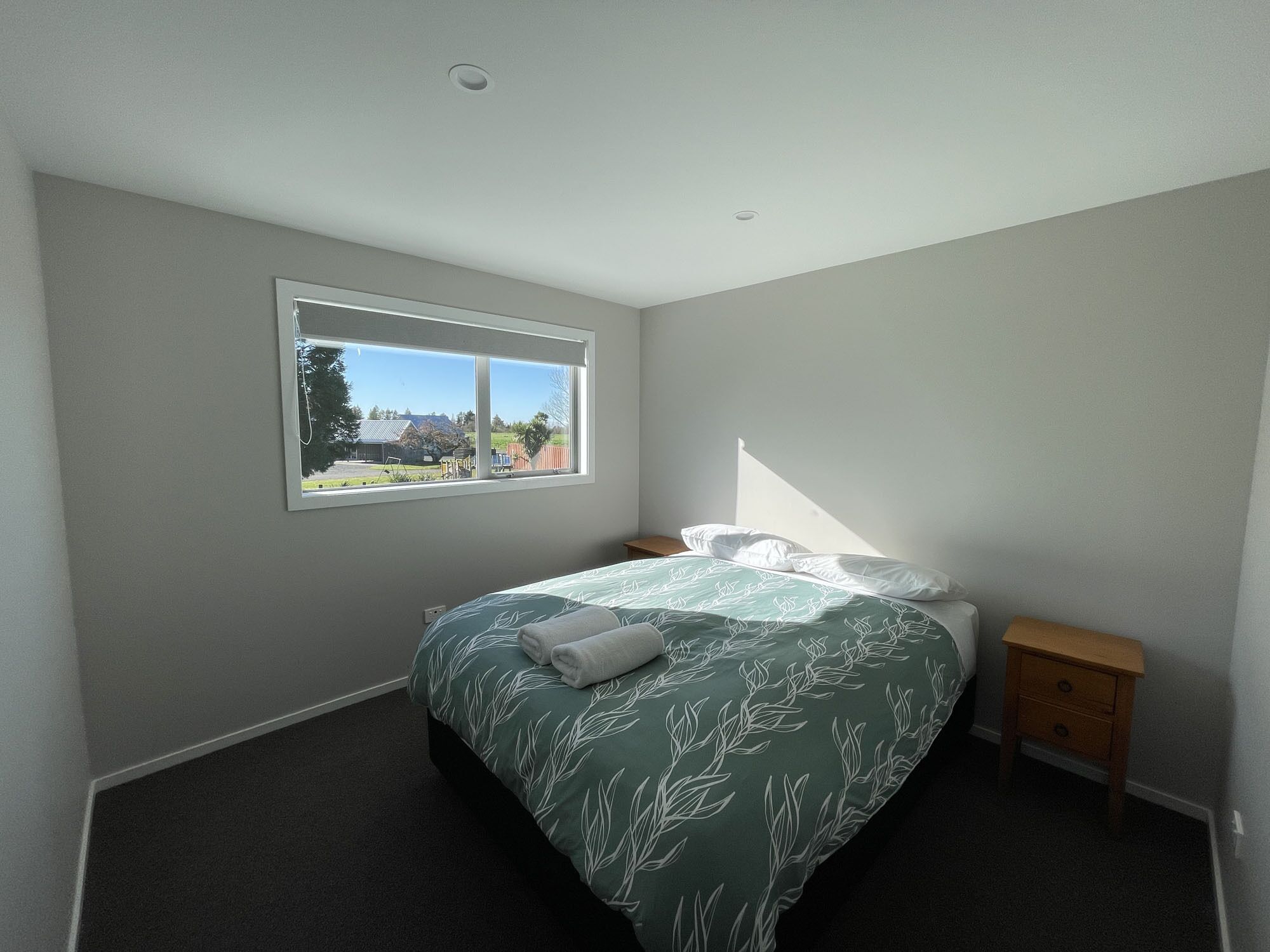 A bedroom with a bed, a nightstand, a window, and a view of the outdoors.