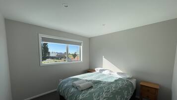 A bedroom with a bed, a nightstand, a window, and a view of the outdoors.