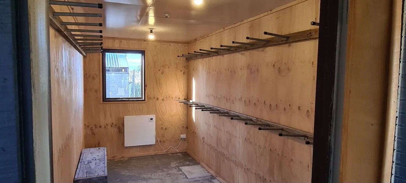 A small, wooden-paneled room with a window, a radiator, and metal racks on the wall.