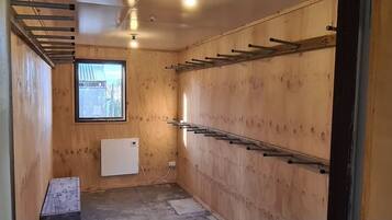 A small, wooden-paneled room with a window, a radiator, and metal racks on the wall.