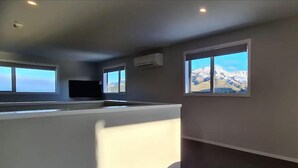 Een moderne kamer met een keukenhoek, grote ramen en uitzicht op bergen.