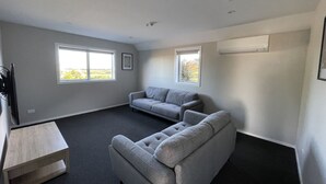 Ein Zimmer mit zwei grauen Sofas, einem kleinen Holztisch und zwei Fenstern, die für natürliches Licht sorgen.