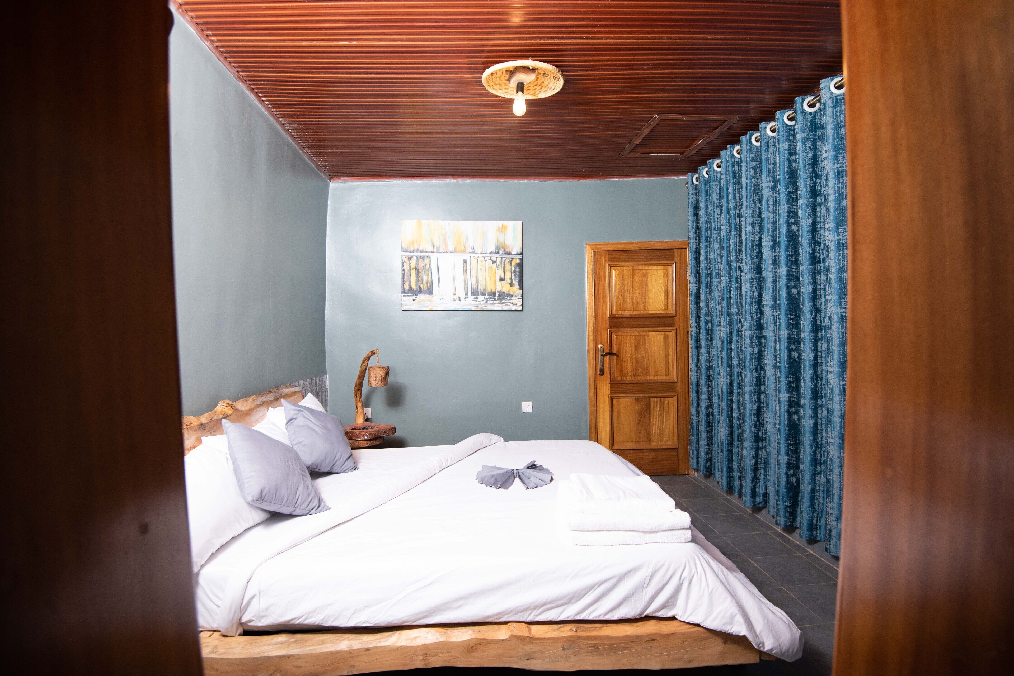 Een slaapkamer met een houten bed, een houten hoofdbord, een wandlamp, een houten deur en een blauw gordijn.