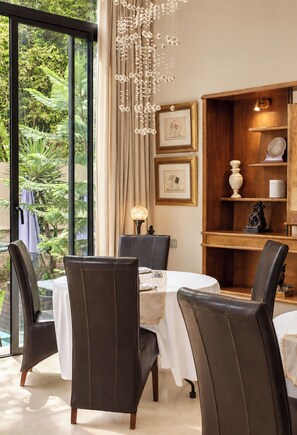 A dining area with a table set for two, surrounded by chairs, with a view of greenery outside. - Sillage Palace Sky & Spa  (Marrakech)