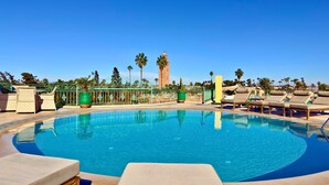 A pool area with lounge chairs, a decorative fence, and palm trees. - Sillage Palace Sky & Spa  (Marrakech)