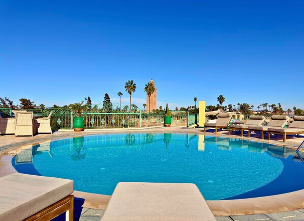 A pool area with lounge chairs, a decorative fence, and palm trees. - Sillage Palace Sky & Spa  (Marrakech)