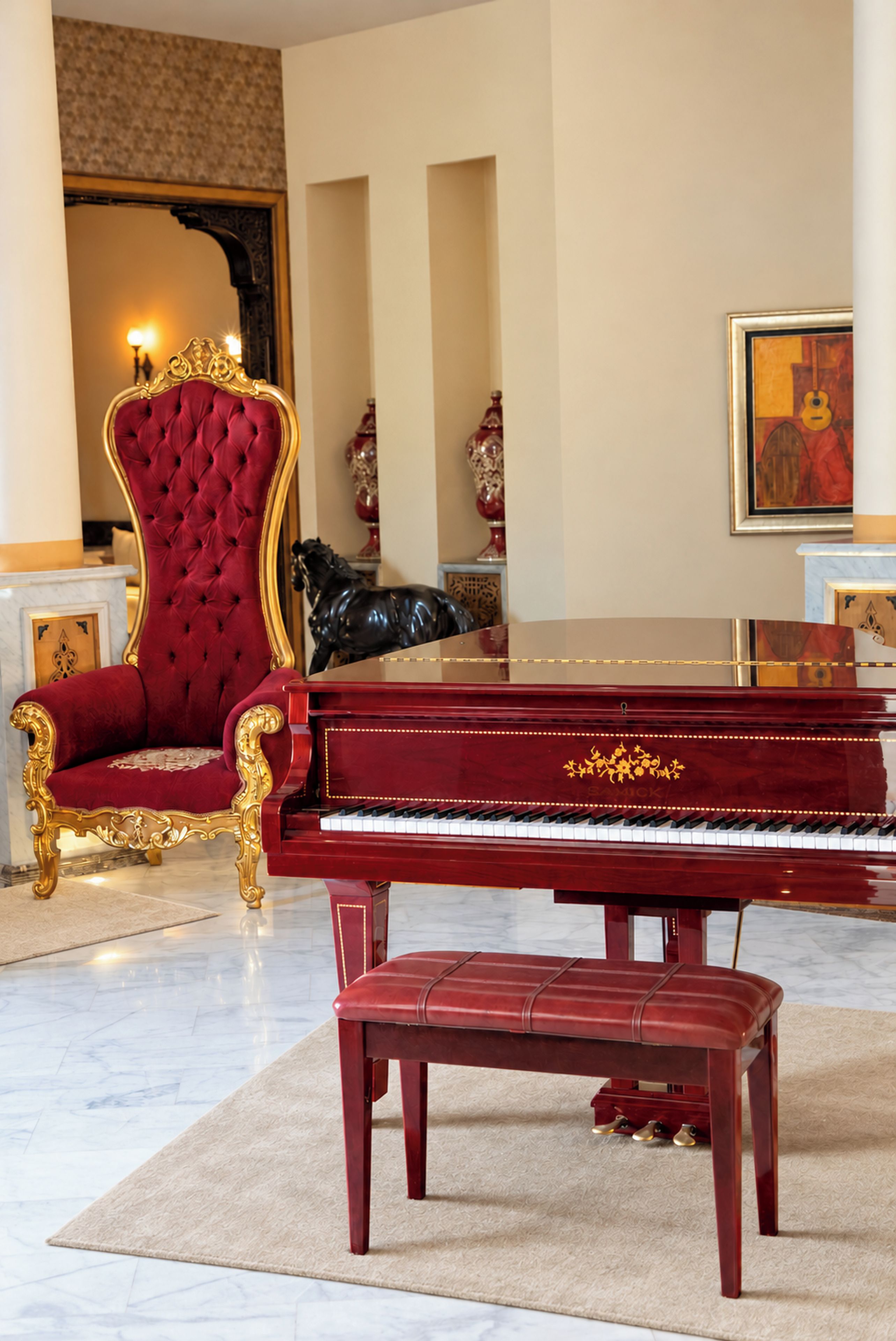 A grand piano, a red upholstered chair, and a marble floor in a room with a large mirror and a painting on the wall.