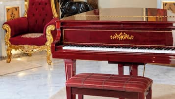 A grand piano, a red upholstered chair, and a marble floor in a room with a large mirror and a painting on the wall.