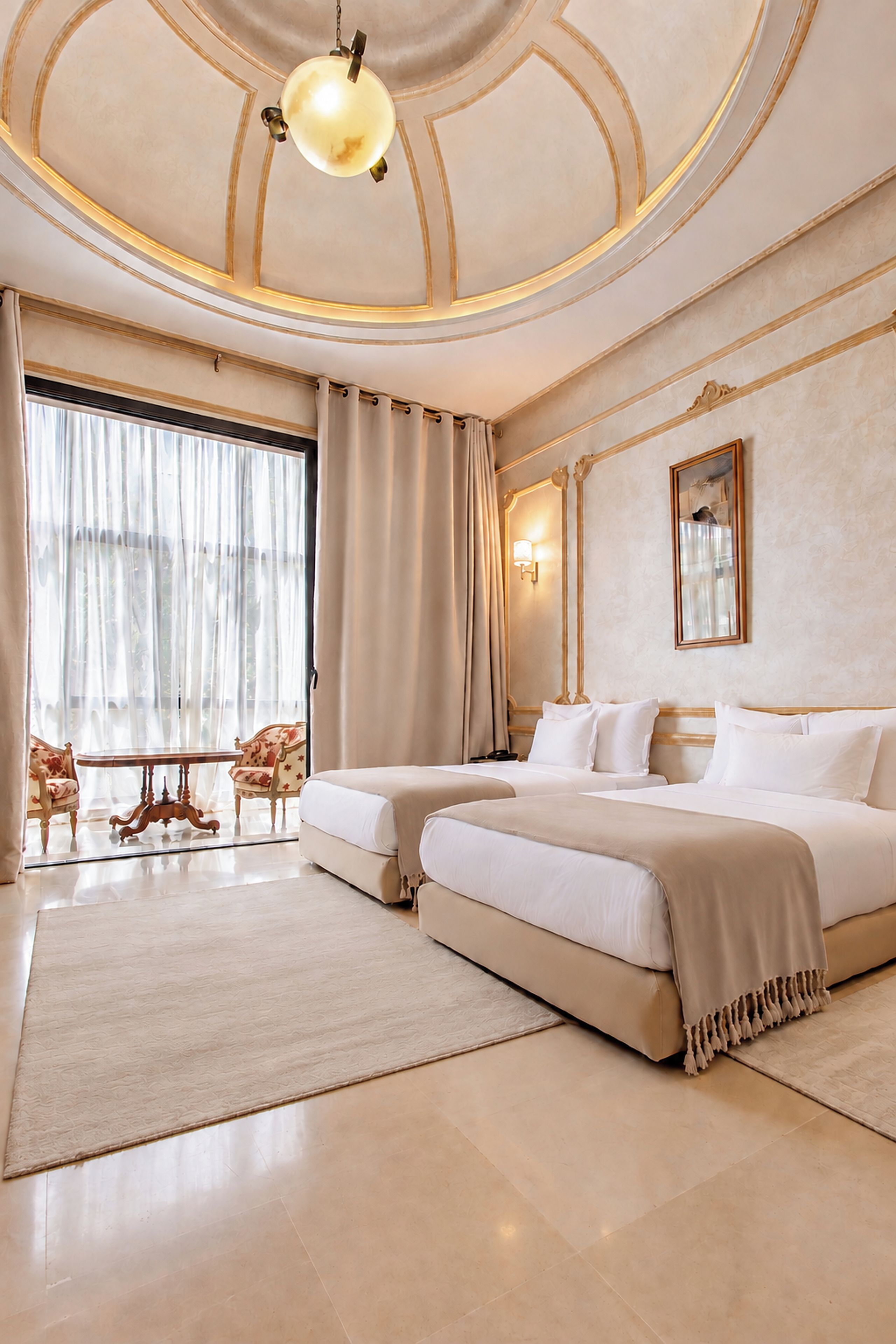 A luxurious hotel room with a large bed, a sitting area with a chair and table, and a large window with curtains.