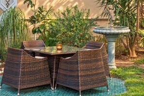 A wicker table and chairs set on a tiled patio with a fountain and greenery in the background. - Sillage Palace Sky & Spa  (Marrakech)