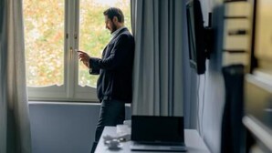 A man standing by a window in a room with a laptop on a table, a chair, and a TV mounted on the wall. - STANDARD APARTMENT (Roma)