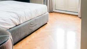 A bedroom with a bed, a radiator, a window with curtains, and a wooden floor. - STANDARD APARTMENT (Roma)