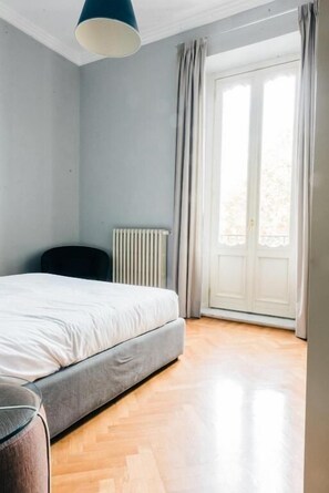 Un dormitorio con cama, un radiador, una ventana con cortinas y suelo de madera.