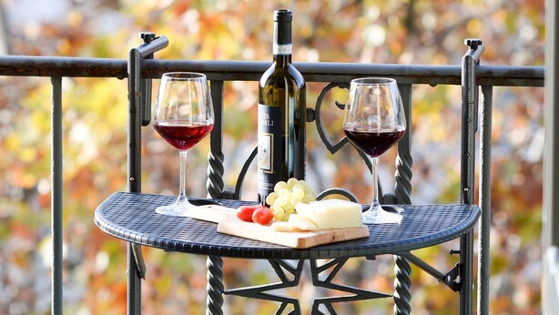 A metal table with a bottle of wine and two glasses on it, set against a backdrop of autumn leaves. - STANDARD APARTMENT (Roma)