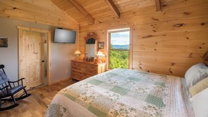 Un dormitorio de cabaña de madera con cama, cómoda, mecedora y televisor en la pared.