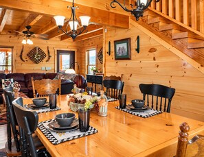 Un interior de madera con una mesa de comedor dispuesta para cuatro personas, sillas alrededor y una escalera que conduce a un nivel superior.