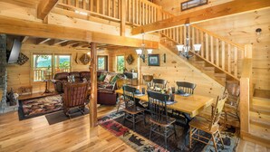 Una cabaña de madera espaciosa con comedor, sala de estar con chimenea y una escalera que conduce a un nivel superior.