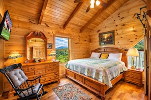 Un dormitorio de cabaña de madera con una cama, cómoda, silla y un ventanal con vistas.