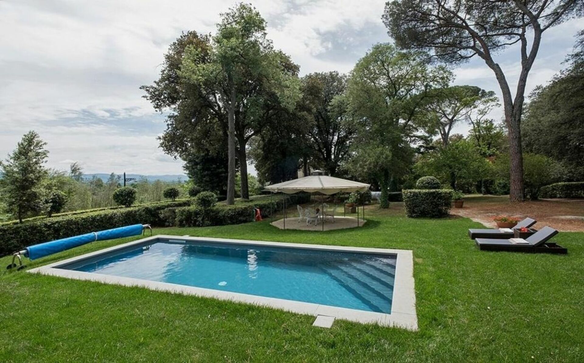 A rectangular swimming pool surrounded by a well-maintained lawn with a gazebo and lounge chairs.