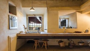 A kitchen with a large island, stools, hanging baskets, and a window with a view.