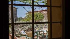 A view through a window with a table and chairs outside, a stone wall, and a building in the background.